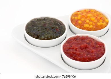 Burger Relish Selection Of Red Tomato, Green Gherkin And Sweetcorn In A Triangular Porcelain Dish With Bowls, Isolated Over White Background.