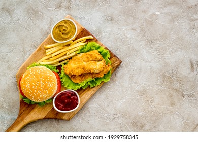 Burger Served With French Fries And Fried Chicken On Wooden Board. Top View