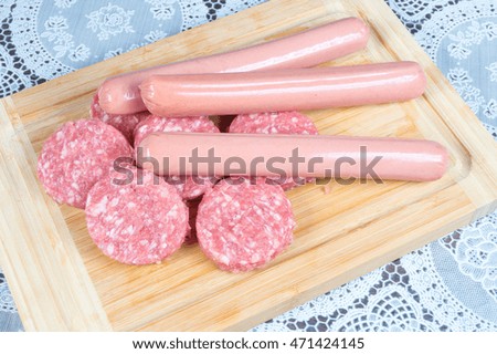 Burgers and dry sausage in the foreground, raw meat