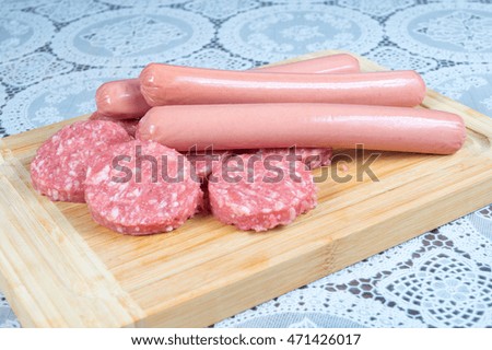 Burgers and dry sausage in the foreground, raw meat