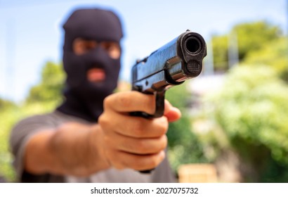 Burglar With Balaclava, Holding A Gun. Man Aiming With A Pistol, Nature Outdoors Background, Closeup View. Intruder, Armed Robber Concept