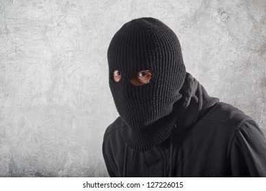 Burglar concept, thief with balaclava caught in front of the grunge concrete wall.
