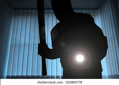 Burglar Or Intruder Inside Of A House Or Office With Flashlight And Baseball Bat