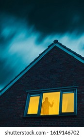 Burglar With Pistol In Eerie House With Illuminated Window Under Stormy Sky At Dusk.