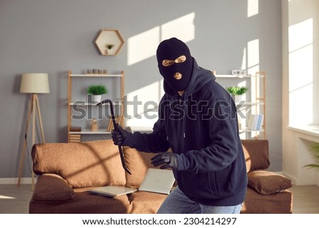 Burglar, robber, thief breaks into somebody's home. Man wearing black balaclava and gloves holding crowbar, walking on tiptoes and looking around for things he can take from this house or apartment