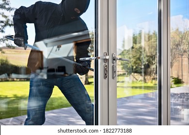 Burglar or thief breaking into a home through window with a crowbar