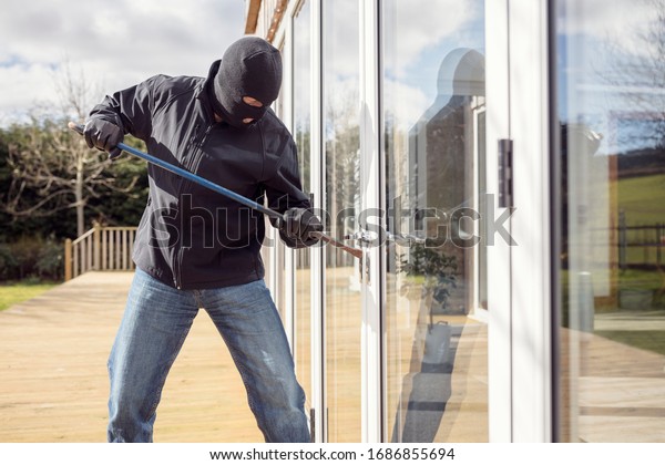 Burglar or thief breaking into a home through\
window with a crowbar
