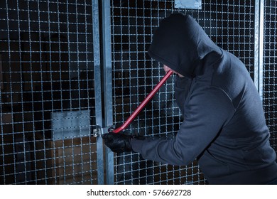 Burglar Trying To Break The Gate Of Storage Room With A Crowbar