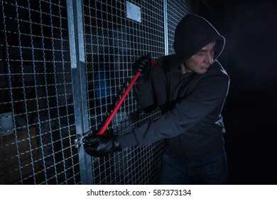 Burglar Trying To Break The Gate Of Storage Room With A Crowbar