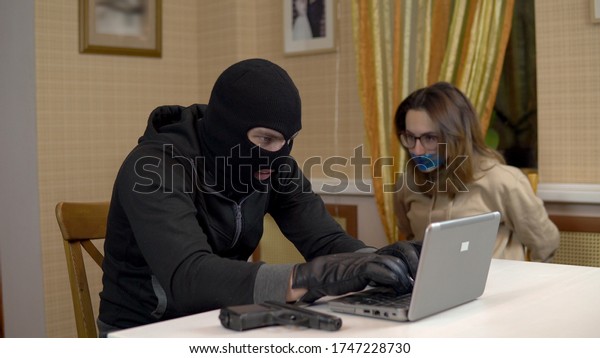 A burglar is trying to break into a laptop by taking a\
young woman hostage. A masked thug sits in a house and cannot break\
into a laptop and threatens a hostage with a gun. Theft of data\
from a