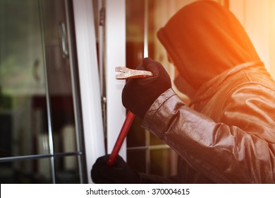Burglar wearing black clothes and leather coat breaking in a house