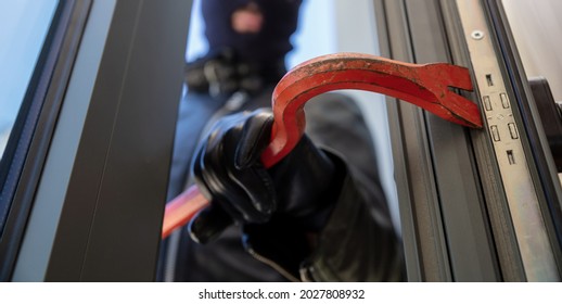Burglary with crowbar. Burglar in balaclava breaking a glass door. Masked housebreaker entering a house for stealing in the daytime. - Shutterstock ID 2027808932