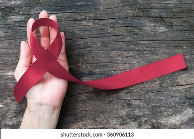 Burgundy ribbon awareness for multiple myeloma cancer awareness and Sickle-Cell Anemia on person's hand support old aged wood (bow isolated with clipping path)