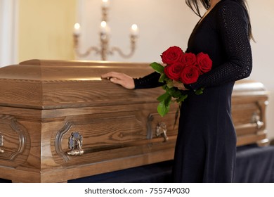 burial, people and mourning concept - unhappy woman with red roses and coffin at funeral in church