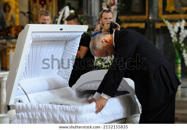 Burial service in a church: man dressed in\
black mourning costume giving his last farewell to the late in\
white coffin. August 10, 2017. Kiev,\
Ukraine