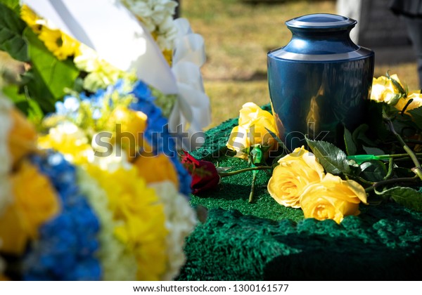 Burial urn\
with yellow roses in a funeral scene, with a floral wreath in the\
foreground, and space for text on the\
left