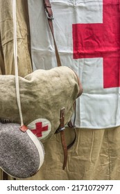 Burlap Bag With A Red Cross And A Flask Against The Background Of A Field Hospital Tent Canvas. A Symbol Of Helping People In Emergency Situations. Closeup Texture Of Canvas And Felt Flask.