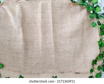 Burlap sackcloth background and texture. Brown natural burlap fabric. Negative space for text decoration. Green artificial leaves frame