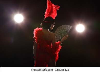 Burlesque dancer with red plumage and red short dress, black and red background, on the stage
