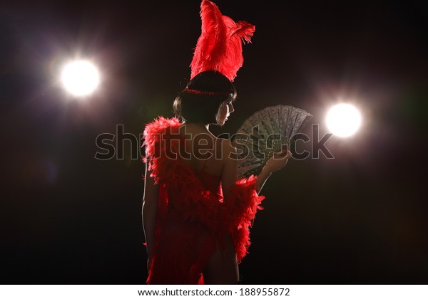 Burlesque dancer with red\
plumage and red short dress, black and red background, on the\
stage