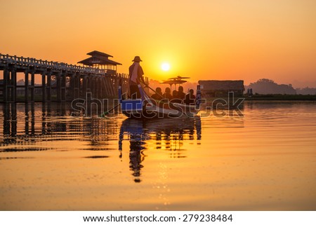 Burmese boatman and buddhist novice sitting in boat, morning sunset in U Bein bridge, Mandalay, Myanmar