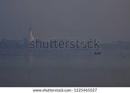 Burmese boatman in U Bein Bridge at sunrise with people crossing Ayeyarwady River, Mandalay, Myanmar