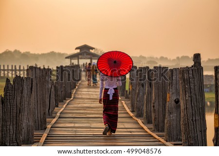 Burmese girl holding a red umbrella walking on U Bein Bridge in the morning in Mandalay, Myanmar.