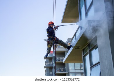 Burnaby Mountain, Vancouver, British Columbia, Canada - July 011, 2018: High Rise Rope Access Window Cleaner Is Power Washing The Building During A Hot Sunny Summer Day.