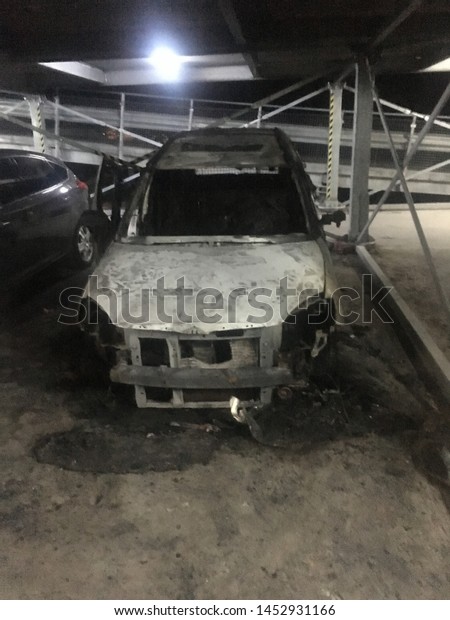 Burned car in a open garage\
from a fire. Insurance evidence and claim proof, low key, phone\
image