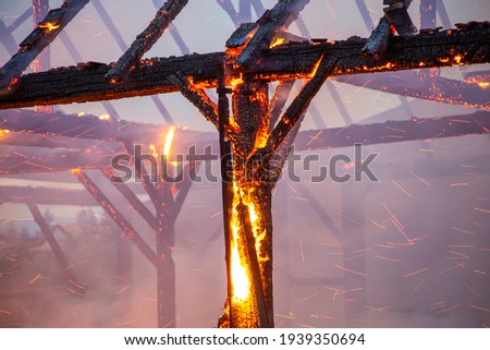 Burned down wooden barn with fire and sparks still blazing. Charred roof truss and wooden posts. burned down wooden framework of a house