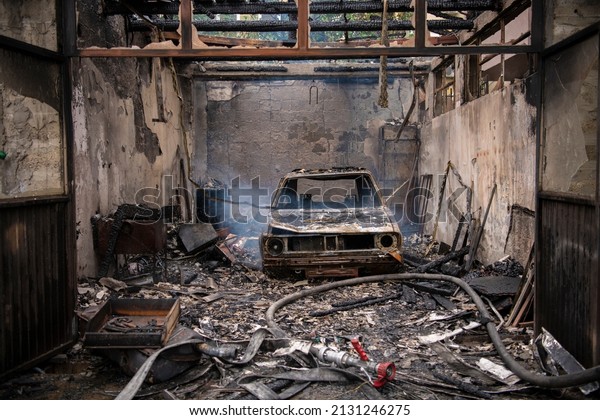 Burned old retro car in a house garage. Explosion\
and fire disaster in workshop. Soot and char all around place. Body\
of the burnt car.