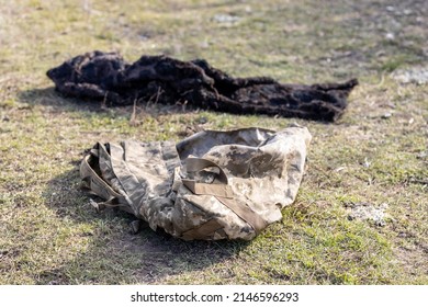 Burned And Torn Piece Of Ukrainian Army Soldier's Pixel Camouflage Military Backpack, He Died In The Village During Battle In A Tank. War Of Russia Against Ukraine. Concept Of Invasion And Genocide. 