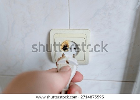 Burned wall socket with a hand extracting a blackened plug, highlighting the aftermath of overheating, faulty wiring and the urgent need for electrical repair.