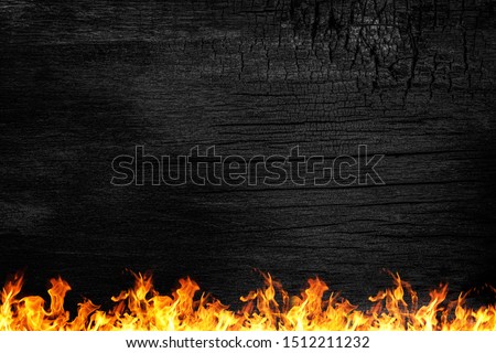 Burning black Board with red fire. Black wooden board and orange flame. Burnt wooden Board texture. Burned scratched hardwood surface. Smoking wood plank background and fire