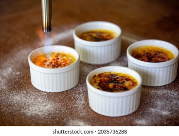 Burning Crème Brûlée With A Blowtorch. Burnt Sugar On Vanilla Cream Surface In Fine Detail In Selective Focus. Selective Focus