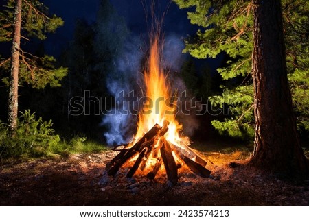 Burning campfire on a dark night in a forest. The bonfire burns in the forest. camp fire in the autumn during vacation in the mountains. Beautiful landscape of nature and trees. Sparks and flames.
