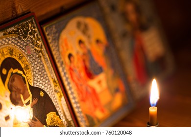 A burning candle against the background of orthodox icons in a dark room