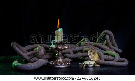 A burning candle in chains on a wooden table and a clock that has stopped time
