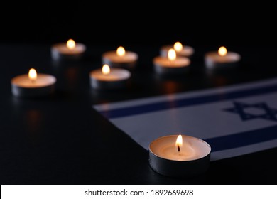 Burning candle and flag of Israel on black table. Holocaust memory day
