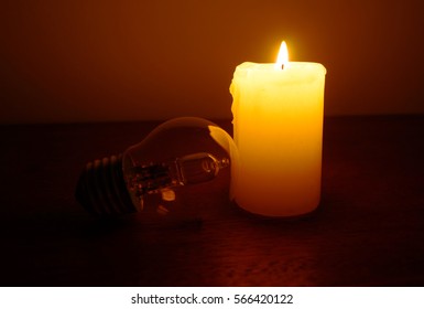 Burning candle and lamp on desktop in darkness (no electricity). Broken electrical wires via storm. Power outage. Blackout.