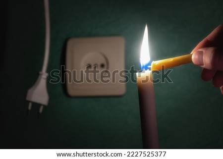 
A burning candle next to an outlet and an electric plug. Blackout, power outage, energy crisis or power outages, conceptual image. Ukraine, the lack of light due to an accident at an electric power