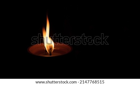Burning candle on a black background. A flame symbolizing a tribute to the dead and fallen. A candle burned in the cemetery on the All Saints' Day. Copy space.