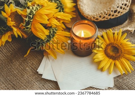 Burning candle, sunflowers, a stack of sweaters and a book.