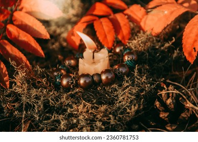 burning candle, a symbol of the moon, an amulet lying on the moss on a dark natural background. pagan wiccan, slavic traditions. Witchcraft, esoteric spiritual ritual . autumn equinox festival.