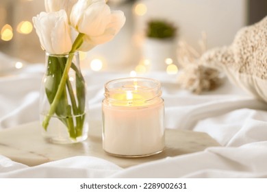 Burning candle and vase with tulips on bed, closeup - Powered by Shutterstock