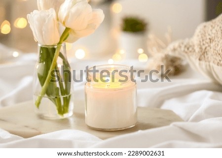 Burning candle and vase with tulips on bed, closeup