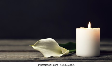 Burning candle and white calla lily on dark background with copy space. Sympathy card  
