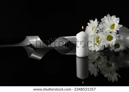 Burning candle, white chrysanthemum flowers and ribbon on black mirror surface in darkness, space for text. Funeral symbols