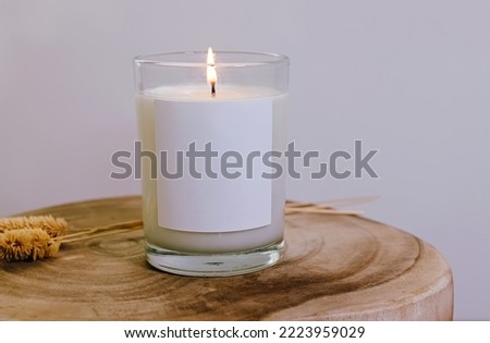 Burning candle with white empty label close-up, mock-up.