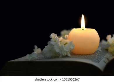 Burning candle and white flowers on opened book  